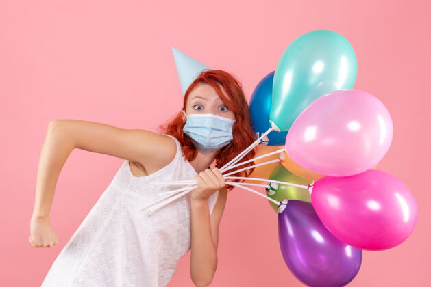 视图正面图年轻女性手持彩色气球在粉红色的面具上庆祝病毒圣诞节