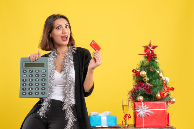 美丽圣诞心情 微笑的美女站在办公室里 手里拿着计算器银行卡 办公室里的黄色肖像成人圣诞节