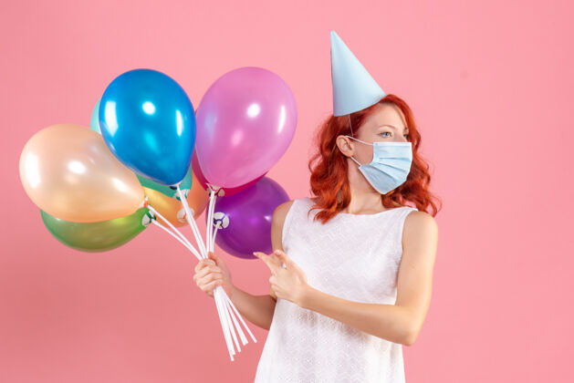 快乐正面图：年轻女性手持彩色气球 戴着粉色的无菌面具生日彩色消毒