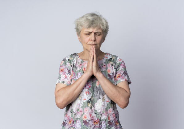 手焦急的老妇人双手合十 闭着眼睛 孤零零地在白墙上祈祷祈祷老人在一起