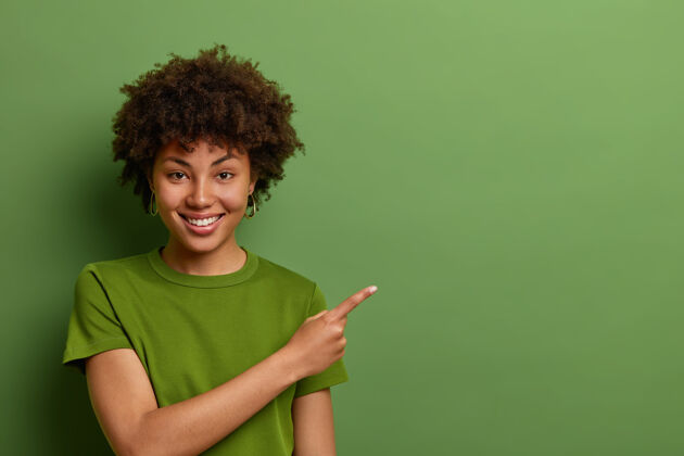黑发面容友好 心情愉快的女店员乐于帮助顾客 在店内指路并演示折扣 将手指放在绿色墙壁上方的空地上时尚颜色促销