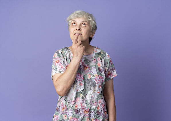紫焦虑的老妇人把手指放在嘴里 看着隔离在紫色墙上起来女人急