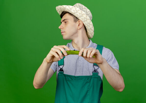 帽子自信的年轻男园丁戴着园艺帽 拿着辣椒看着隔离在绿色背景和复制空间的一边举行绿色空间
