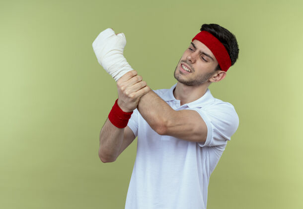 触摸戴着头巾的年轻运动型男子站在绿色背景上 摸着缠着绷带的手感到疼痛运动绷带疼痛
