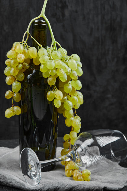 葡萄酒白葡萄围绕着一瓶葡萄酒和一个空杯子在黑暗的背景下高品质的照片保存有机新鲜