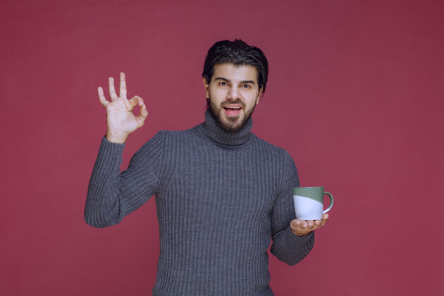 年轻穿着灰色毛衣的男人拿着咖啡杯 享受着咖啡的味道休闲阳刚巧克力