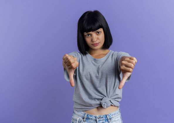 年轻年轻的黑发白人女孩拇指朝下 两只手孤立地放在紫色背景上 留有复印空间黑发女孩复制
