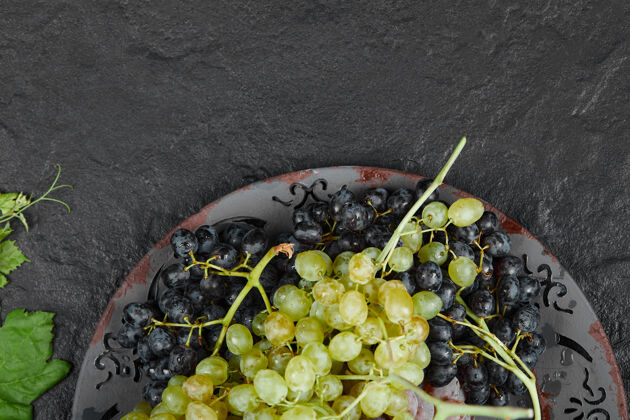 新鲜一盘深色背景上有叶子的混合葡萄高质量的照片季节成熟陶瓷