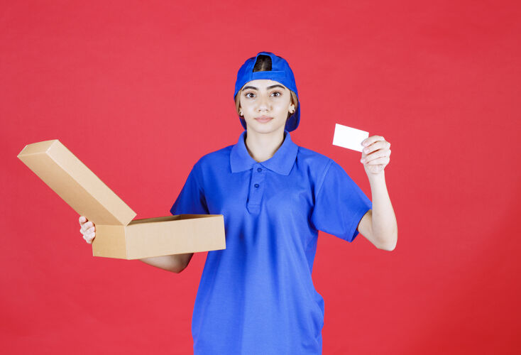 服装穿着蓝色制服的女快递员拿着一个纸板外卖箱 出示她的名片联系人姿势电子邮件