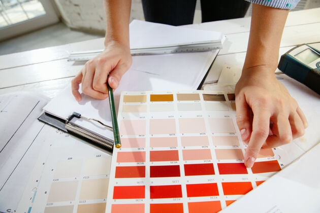 油漆专业的室内设计师或建筑师 在现代办公室中使用调色板和房间图纸年轻的女模特规划未来的公寓或房子 选择颜色和位置建筑师桌子男性