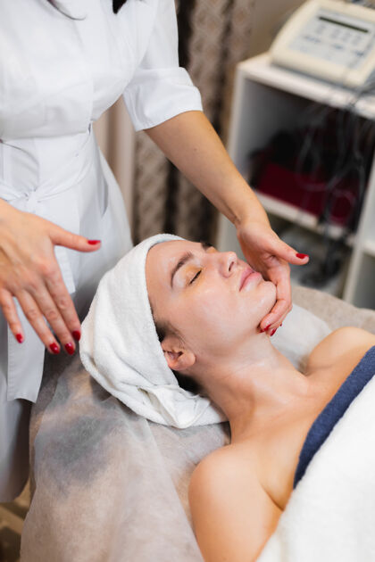 女人一家spa美容院的美容师在顾客脸上涂上面霜 一个女孩躺在美容台上美容医学过程
