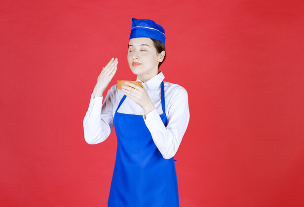 东方人穿着蓝色围裙的厨师拿着一个陶碗 闻着味道聪明人美食家年轻人