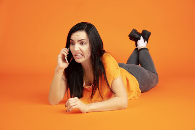 行政橙色工作室背景上的白种人年轻女子肖像穿着衬衫的漂亮黑发女性模特人类情感的概念 面部表情 销售 广告广告空间电话交谈人财务工作
