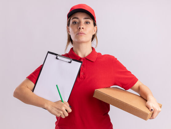 人自信的年轻漂亮的女送货员穿着制服拿着比萨饼盒和剪贴板隔离在白墙上站信心漂亮