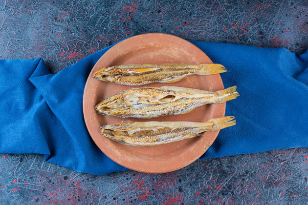 咸把咸鱼干放在一块粘土板上 背景是深色的干海鲜木板