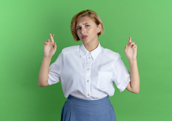 焦虑年轻焦急的金发俄罗斯女孩交叉手指在绿色背景与复制空间孤立金发女孩俄国人