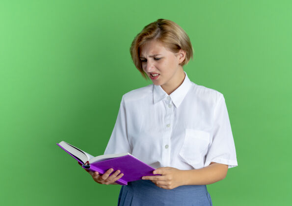 困惑年轻迷茫的金发俄罗斯女孩抱着书 看着书 书的背景是绿色的 还有复印空间金发碧眼年轻女孩