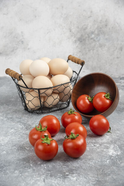 早餐柳条篮子的生有机鸡蛋和一碗西红柿放在大理石上食物蔬菜生的