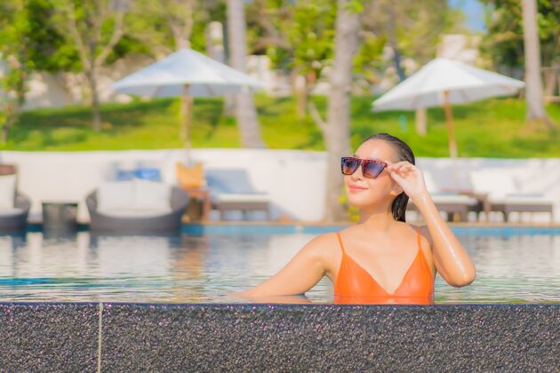 中国肖像美丽的亚洲年轻女子放松微笑休闲周围的室外游泳池在度假酒店海景比基尼肖像帽子