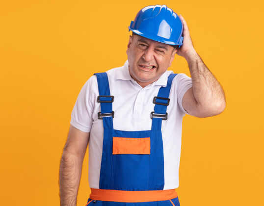 站着疼痛的成年建筑工人穿着制服 把头孤立地放在橙色的墙上人人抱着