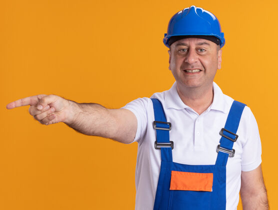 建设者微笑的成年建筑工人身着制服 站在隔离的橙色墙上脸衣服壁板