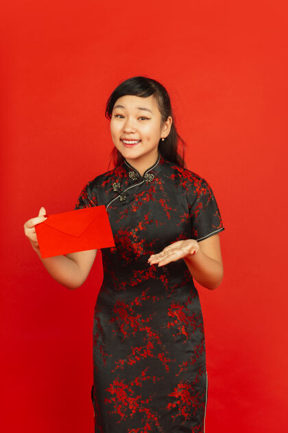 手2020年中国新年红色背景上孤立的亚洲少女肖像身着传统服装的女模特看起来很开心 微笑着 拿着红包庆祝 节日 情感广告照明服装