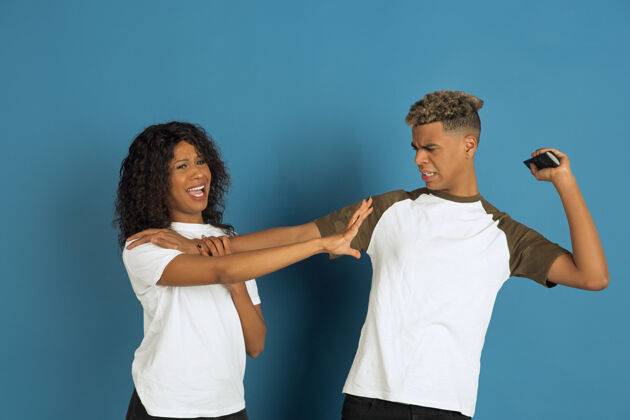 选择年轻感性的非裔美国人 穿着白色休闲服 在蓝色背景上摆姿势美丽的情侣人类情感的概念 面部表情 关系 广告一起看电视金融面部衣服