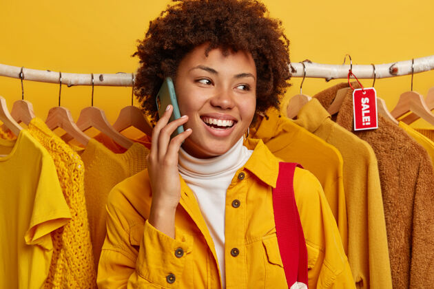服装开朗的非洲裔美国妇女在手机上交谈 在商店里检查一些衣服 在衣架上摆姿势 分享商店里的销售情况电话美式购物狂