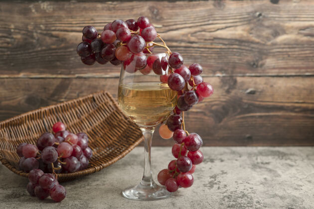 红柳条筐的红葡萄和一杯葡萄酒放在大理石桌上酒精新鲜集群