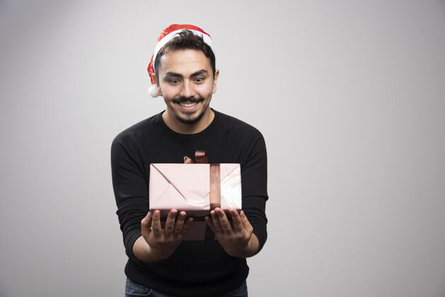 圣诞老人一个年轻人拿着一个礼品盒在灰色的墙上圣诞老人站圣诞