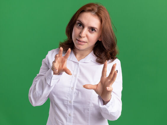 手势身穿白衬衫的年轻女子看着前面做爪子的手势 一只猫微笑着站在绿色的墙上年轻衬衫微笑