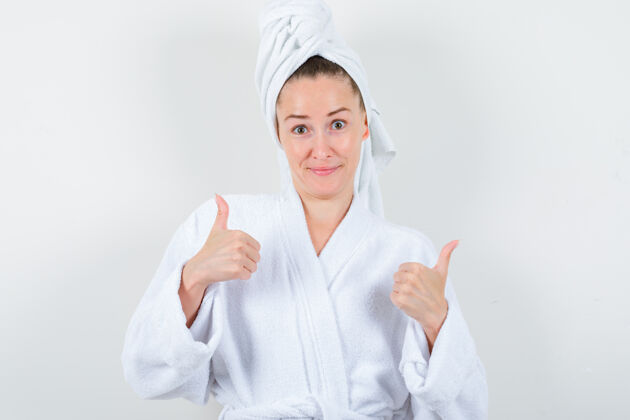 女性身着白色浴衣 毛巾的年轻女士向上竖起大拇指 看上去很愉快 正面视图皮肤护理毛巾完美