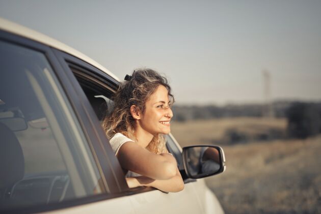 头发一个微笑的年轻女子从车里向外看的特写镜头道路车轮汽车