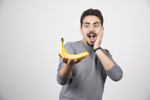 人黑发男人高兴地看着香蕉微笑时尚姿势