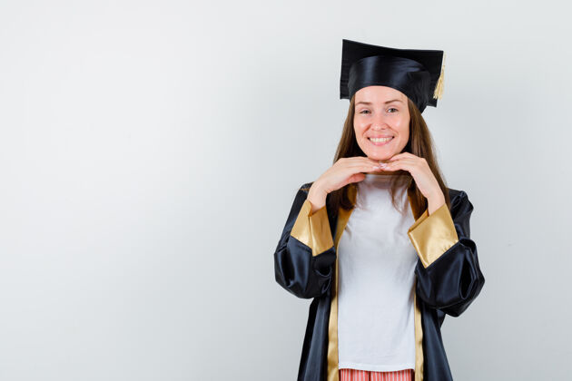 大学女毕业生穿着学院服 双手放在下巴下面 看起来很快乐正面图Cap学术成人
