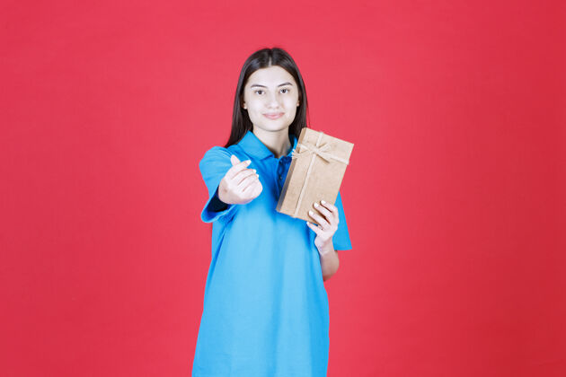 女人穿着蓝色衬衫的女人拿着一个纸板小礼盒 做着手指心的手势生日人手指心手势