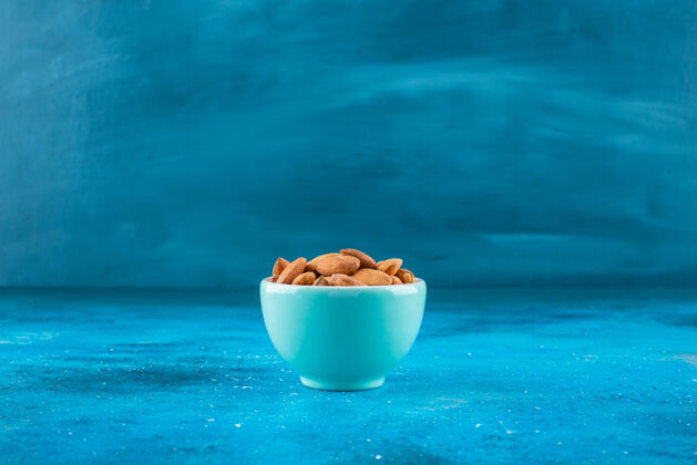 美味在蓝色表面的碗里放着没有壳的杏仁营养坚果自然