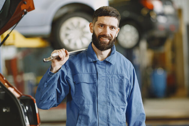 微笑一个穿着工作服 拿着工具的男人在汽车旁边的车库里维修车库工作