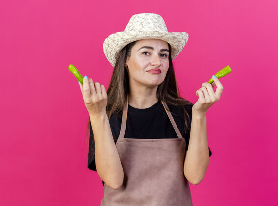 制服穿着制服的漂亮的园丁女孩戴着园艺帽 手里拿着一个粉红色背景上孤立的破胡椒不愉快女孩园艺