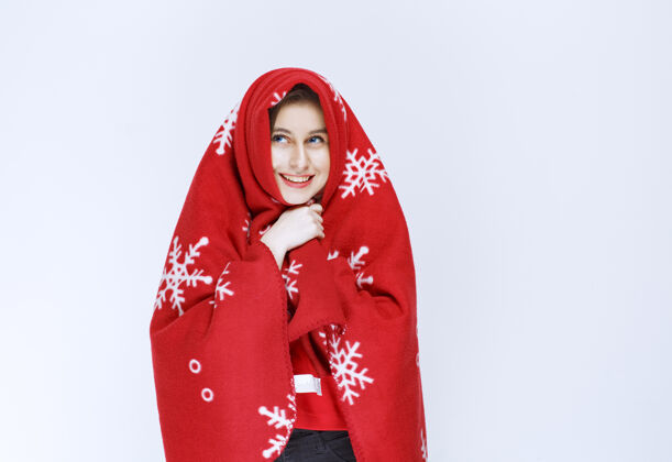 年轻一个年轻的女人用一条红色的暖和的毯子盖着自己孤立羊毛冬天