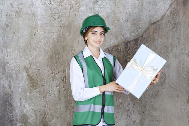 工作场所身着绿色制服 头戴安全帽 手持蓝色礼盒的女工程师人工程师庆典