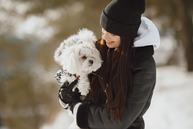 肖像在冬季公园散步的可爱女孩穿着棕色夹克的女人牵着狗的女人玩女性欢呼