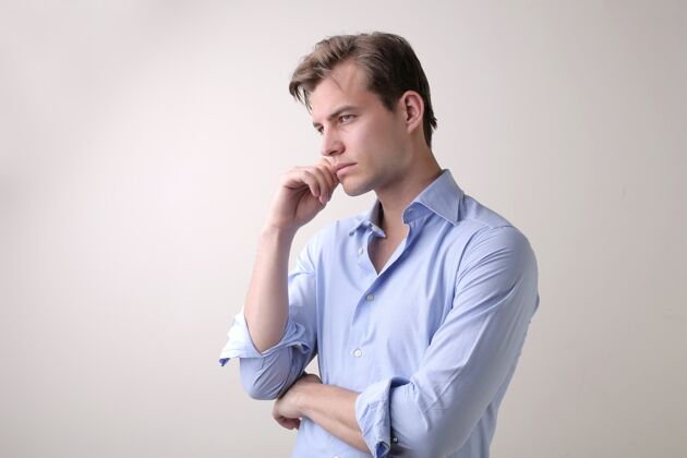 手一个穿着蓝色衬衫的年轻男人站在一堵白色的墙上 有着深刻的思想衬衫年轻头发