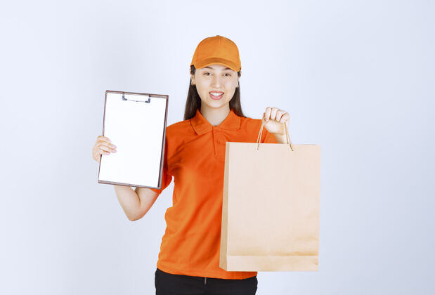 员工身着橙色制服的女服务人员手持一个硬纸板购物袋 向顾客出示签名单发货女士工人