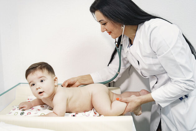 儿童带听诊器的女人尿布里的婴儿肚子上躺着的婴儿医学护理评级