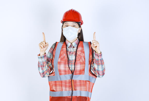 方向戴着红色头盔和安全面具的女建筑工程师员工新常态工作场所