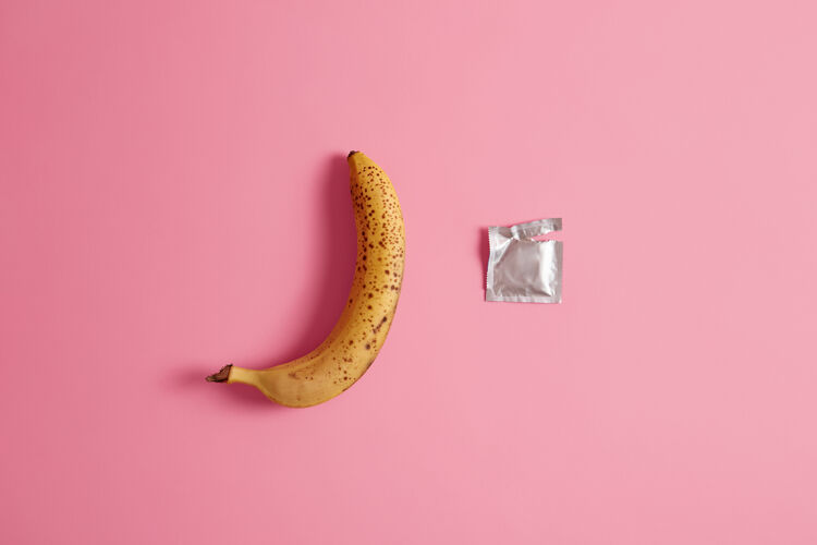 扁平打开包装的避孕套和一整根香蕉放在粉红色的工作室背景上避孕药 预防性病 预防怀孕 避孕可逆的 临时的避孕方式避孕药品乳胶