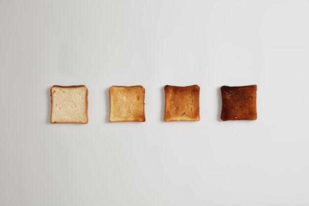 烤四片面包片 从未吃到烧焦 放在烤面包机里 靠着白色的表面排成一排一套烤面包片 用来做美味的硬皮三明治美味的早餐 烹饪食物新鲜卡路里块