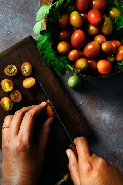 番茄一个人在桌上的木板上切新鲜的樱桃西红柿的俯视图板食物切片