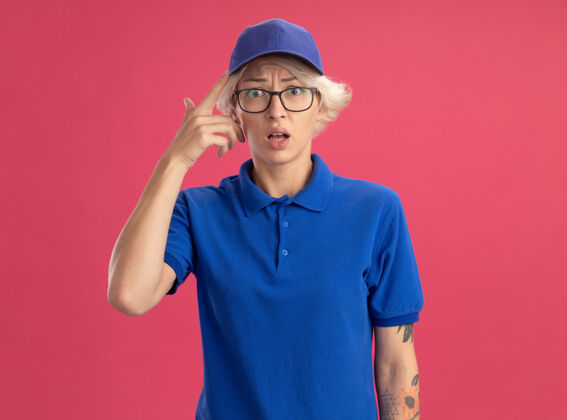 年轻穿着蓝色制服 戴着帽子的年轻女送货员被粉红色的墙壁弄糊涂了 非常焦虑焦虑分娩帽子